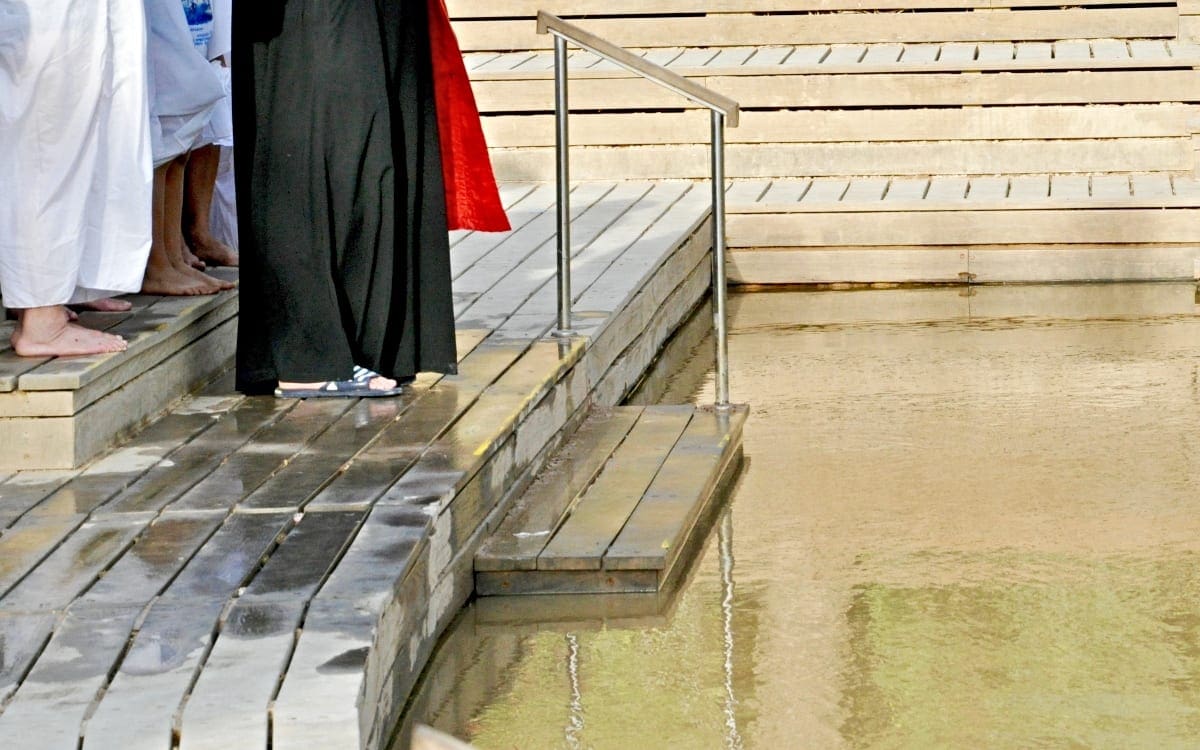 The feet of several people standing at the traditional site of Jesus’ baptism in the Jordan River.