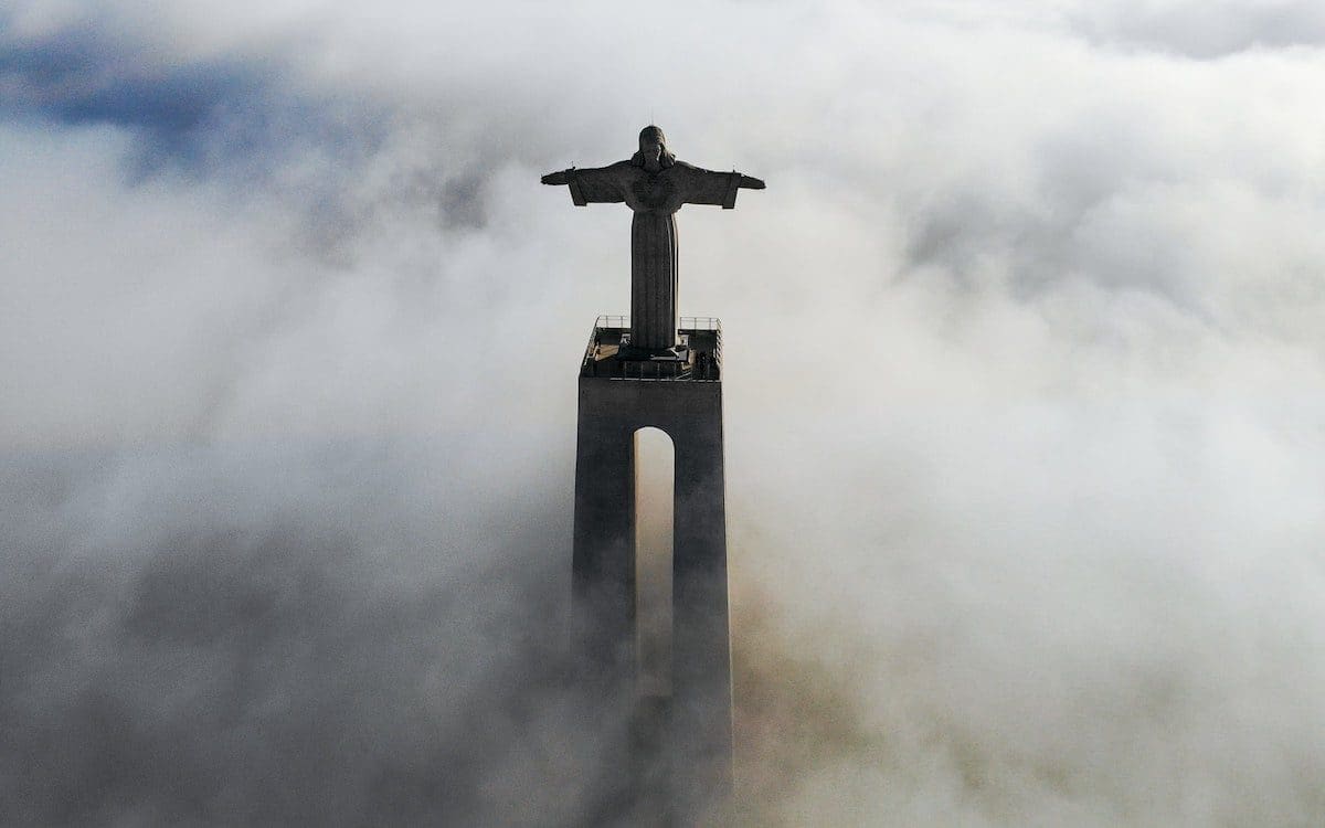 A statue of Jesus rising out of the fog view from above.