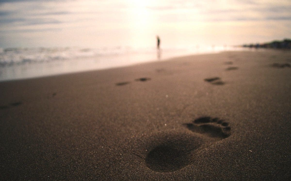 Footprints on a beach with the sun rising in the background.