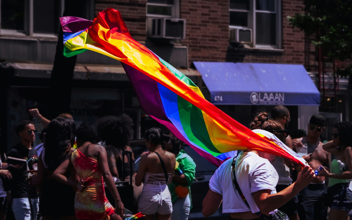 A person draped in a pride flag that is waving in the wind.