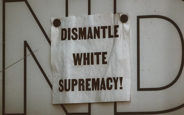 “Dismantle White Supremacy!” printed on paper on a black and white lettered backdrop.